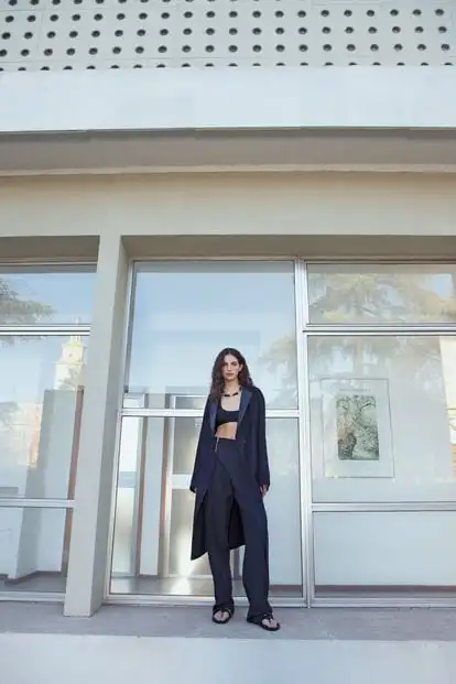 Wool and mohair trench with lambskin collar, ribbed silk knit crop top, wool and mohair pants with zippers, black calfskin and metal necklace, woven calfskin sandals.