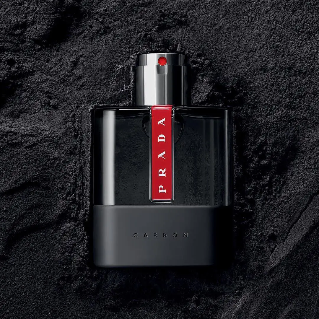 a bottle of luna rosa carbon by prada half buried in the sand