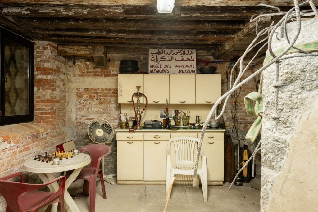 a wooden basement room that is dusty and has sand bags and old plastic chairs and fans and hookah pipes