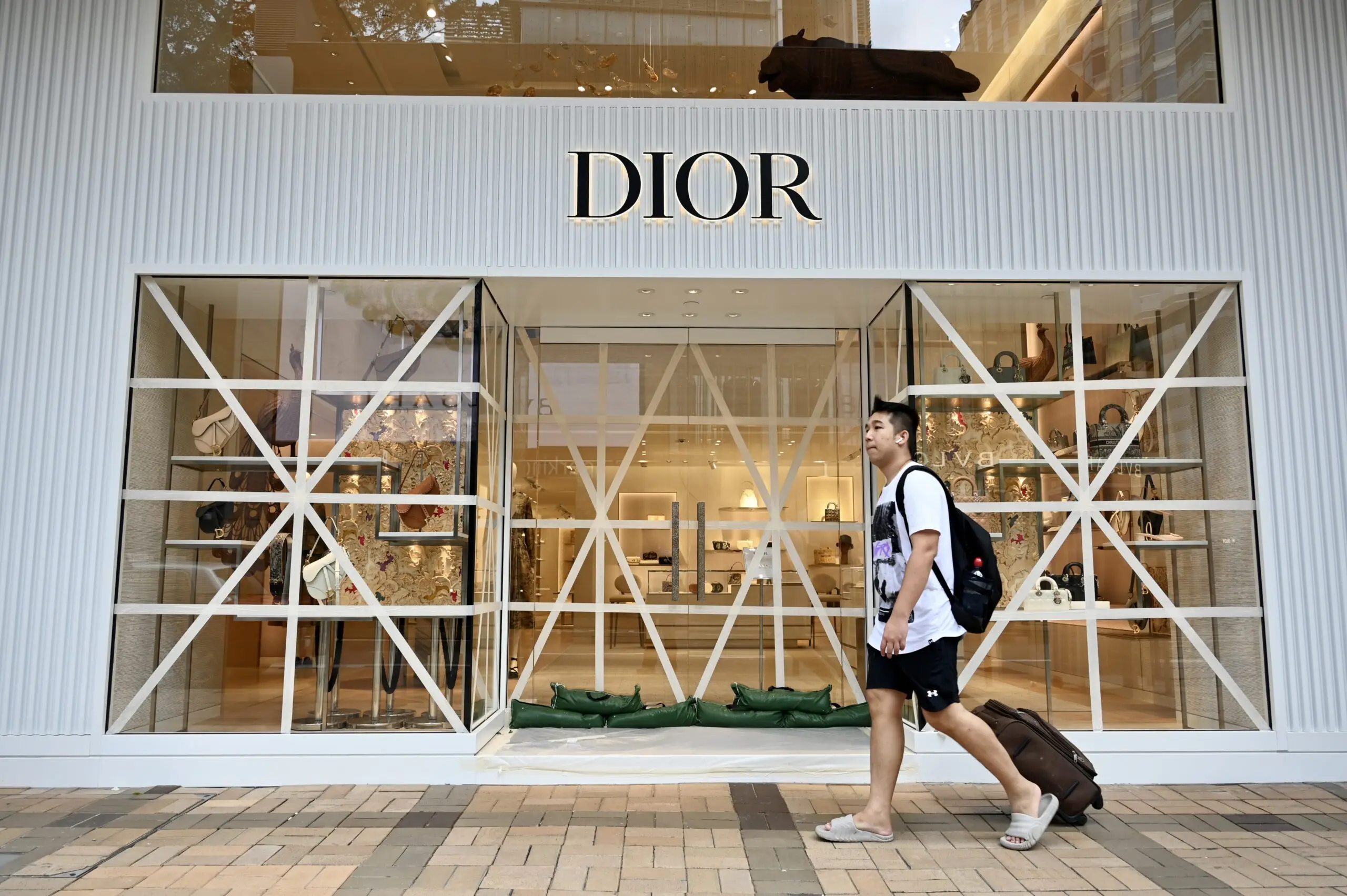 HONG KONG, CHINA – JULY 17: A man walks by taped windows at a Dior store as typhoon Talim passes the city on July 17, 2023 in Hong Kong, China. (Photo by Li Zhihua/China News Service/VCG via Getty Images)