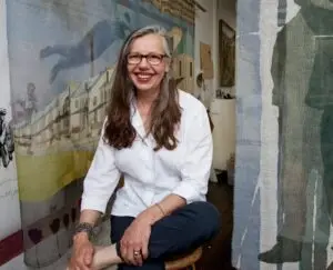 Drop cloths fabricated from textiles are draped behind artist Deborah Baronas. Her exhibition inspired by working-class Americans is opening at the Jamestown Arts Center.