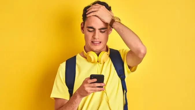 Teenager boy wearing headphones and using smartphone over isolated background stressed with hand on head, shocked with shame and surprise face, angry and frustrated. Fear and upset for mistake. stock photo