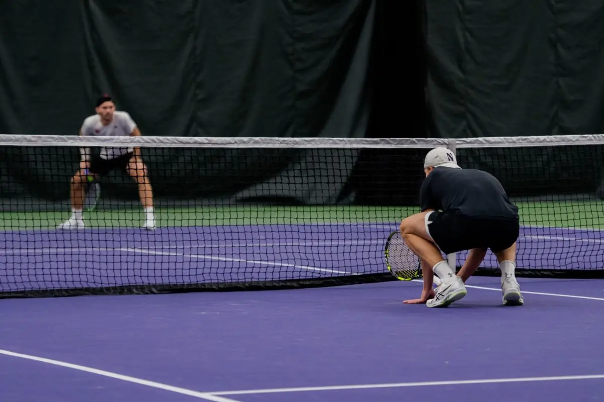 Felix Nordby crouches on the ground in front of the net while holding a tennis racket in preparation for the match.