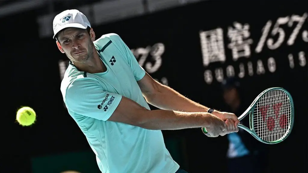 Hubert Hurkacz hits a backhand shot wearing a white shirt and white cap