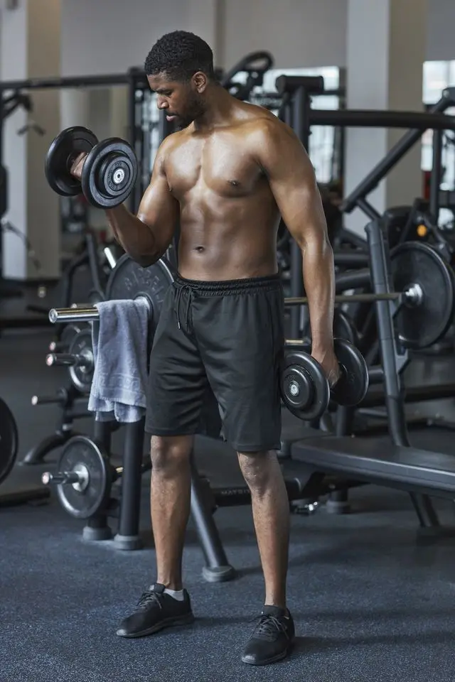 shirtless man exercising with dumbbells in health club