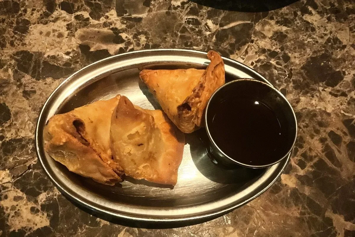 A plate with three samosas and a dish of sauce