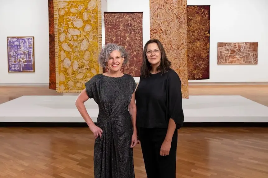 Curators Kelli and Hetti standing in front of batik artworks in the exhibition
