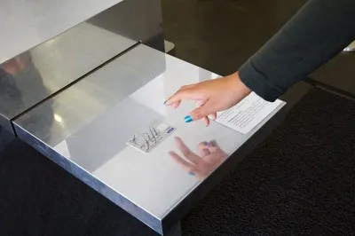 A hand with blue nail polish hovers above a gift credit card lying on reflective metal surface.