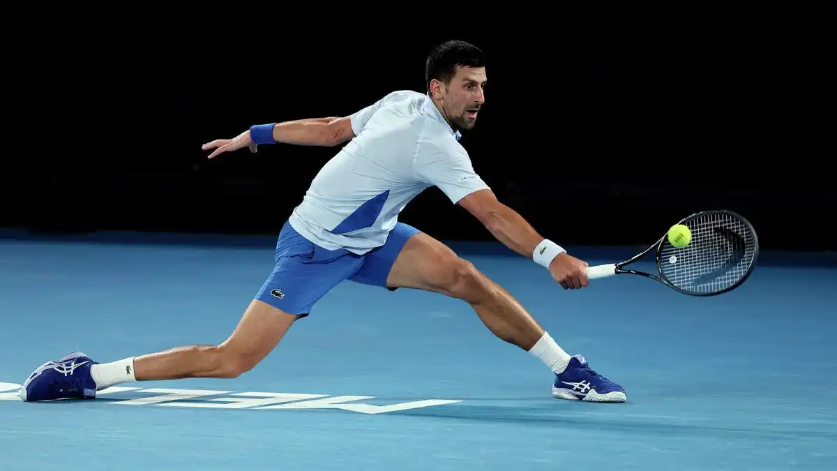 Tennis player fully outreached, trying to reach the ball with his right hand.