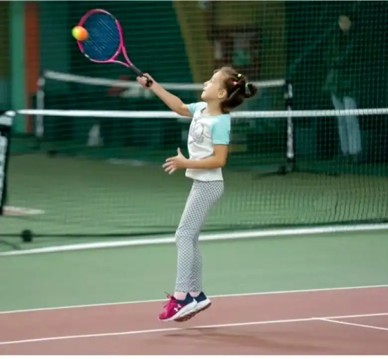 A young girl jumping in the air with a tennis racket to hit a ball