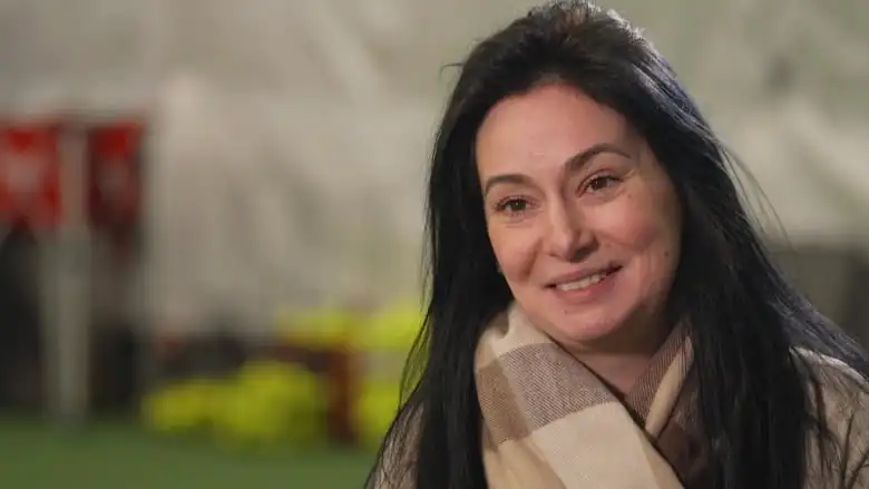 A smiling woman with long black hair, wearing a plaid beige scarf