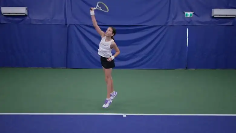 A young girl jumping up in the air with a tennis racket