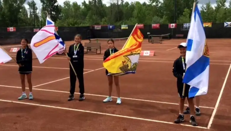 Four kids standing on a tennis court and holding large flags.