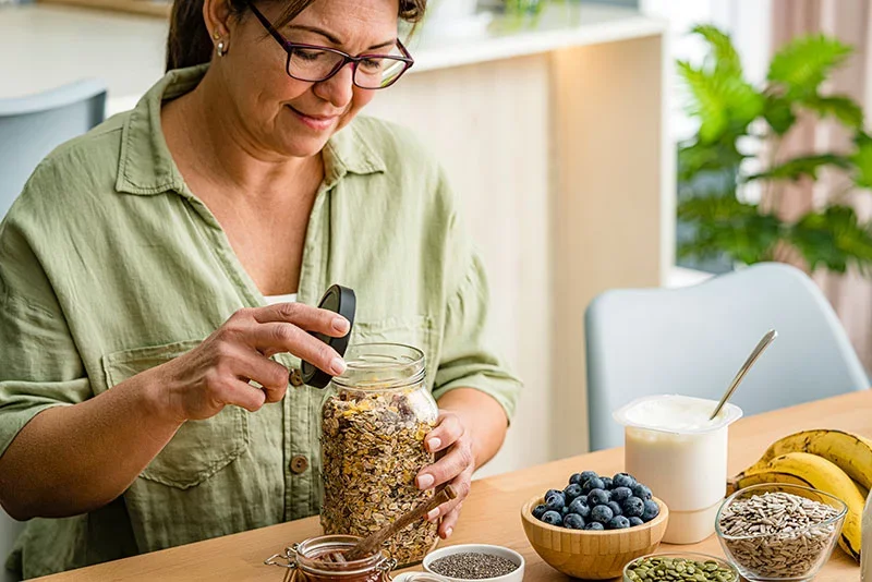 Woman filling a jar with oats. People should try to get fiber through diet and food rather than through supplements or fiber gummies. 