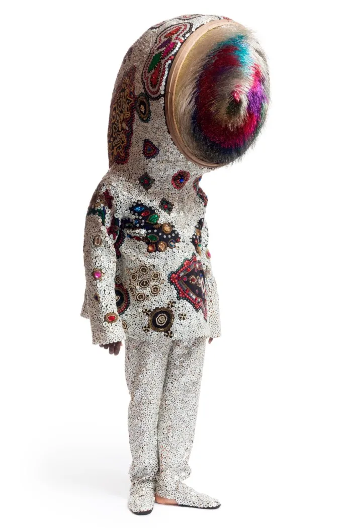 A man in a suit with a giant eye made of mixed media including fabric, buttons, antique sifter, and wire