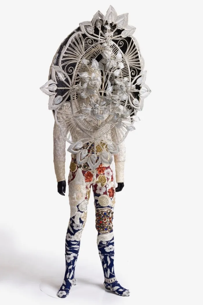 A man in a suit with a giant headpiece made of mixed media