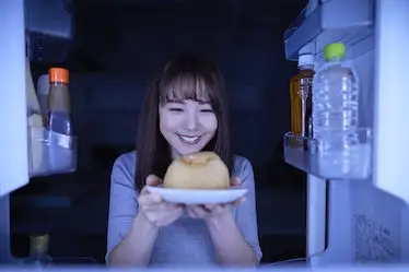 Young Japanese woman eating night snack from the fridge