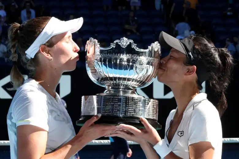 Two women kiss a large silver trophy.