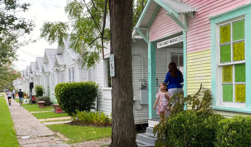 A child and adult standing in the doorway of a house that is part of a row of shotgun-style homes painted white