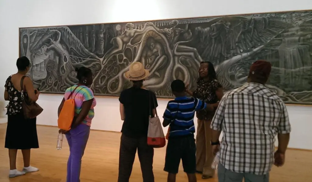 Patrons stand around a large-scale artwork as a docent discusses