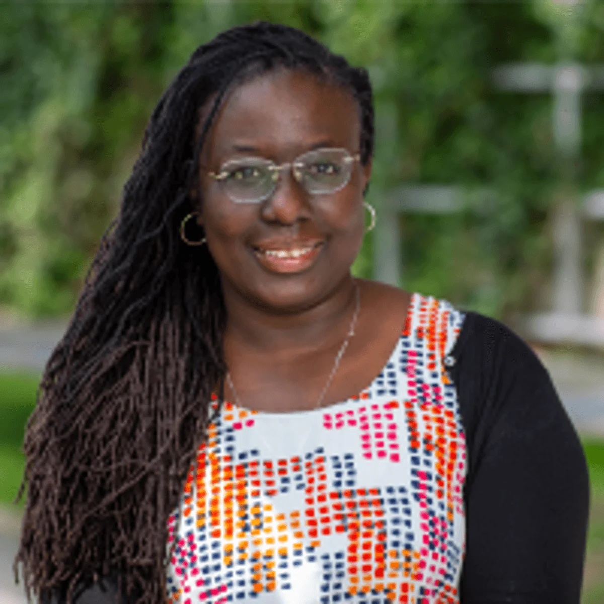 Adama Marie Sesay stand outside and wears glasses, a colorful shirt, and a black sweater.