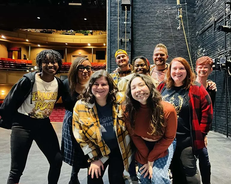 A cast of actors poses on stage