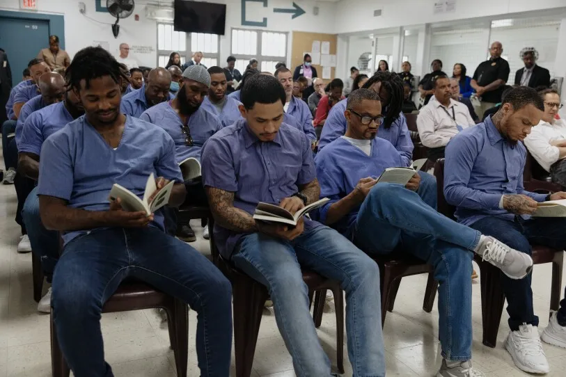 Men in jeans and blue shirts sit and read in Dorsey Run Correctional Facility