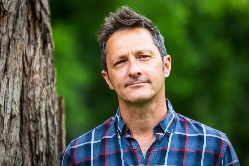 Professor Brendan Wintle stands in front of a tree tree, with green leaves to the side of him