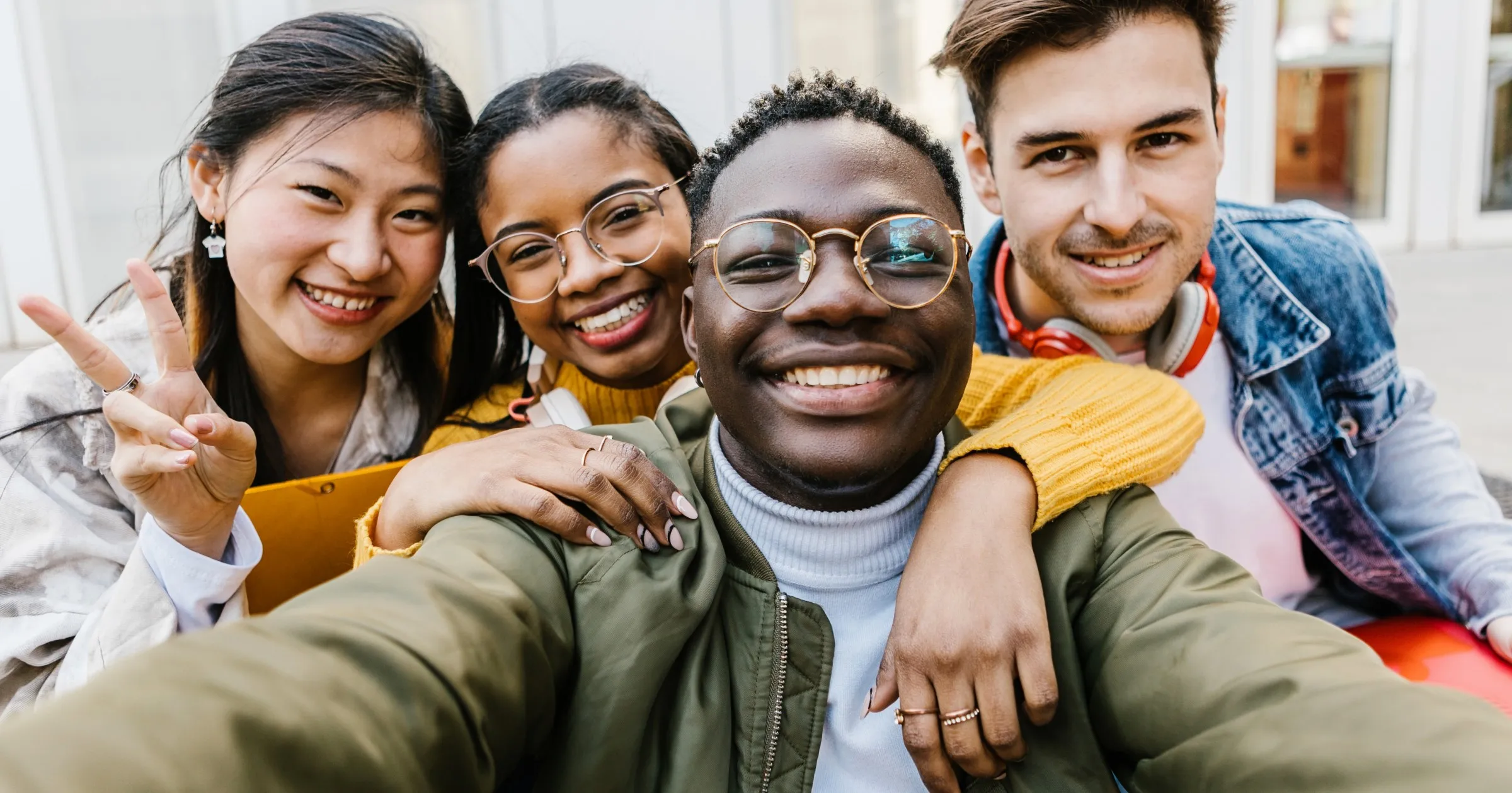 Selfie of four people smiling, person holding camera with two hands in middle of group