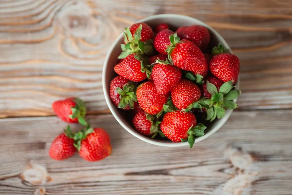 view from the top of a bowl of ripe strawberries, standing on a wooden tableclose up