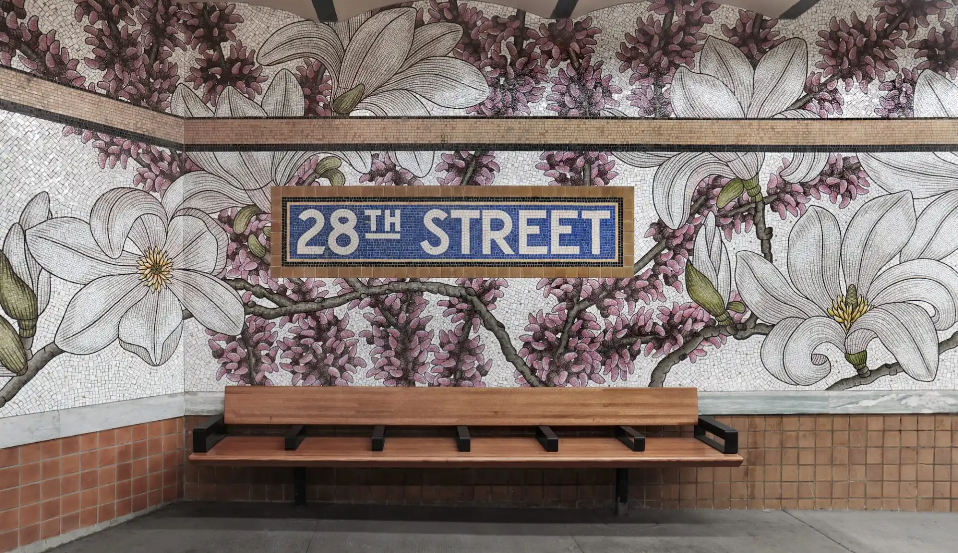 A mosaic in a New York City Subway station showing a tiled sign that reads 28th Street above a bench, and the wall is covered in florals.