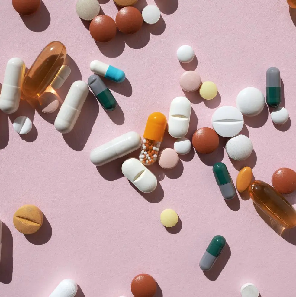 top view of spoon with various pills and tablets on the pink background