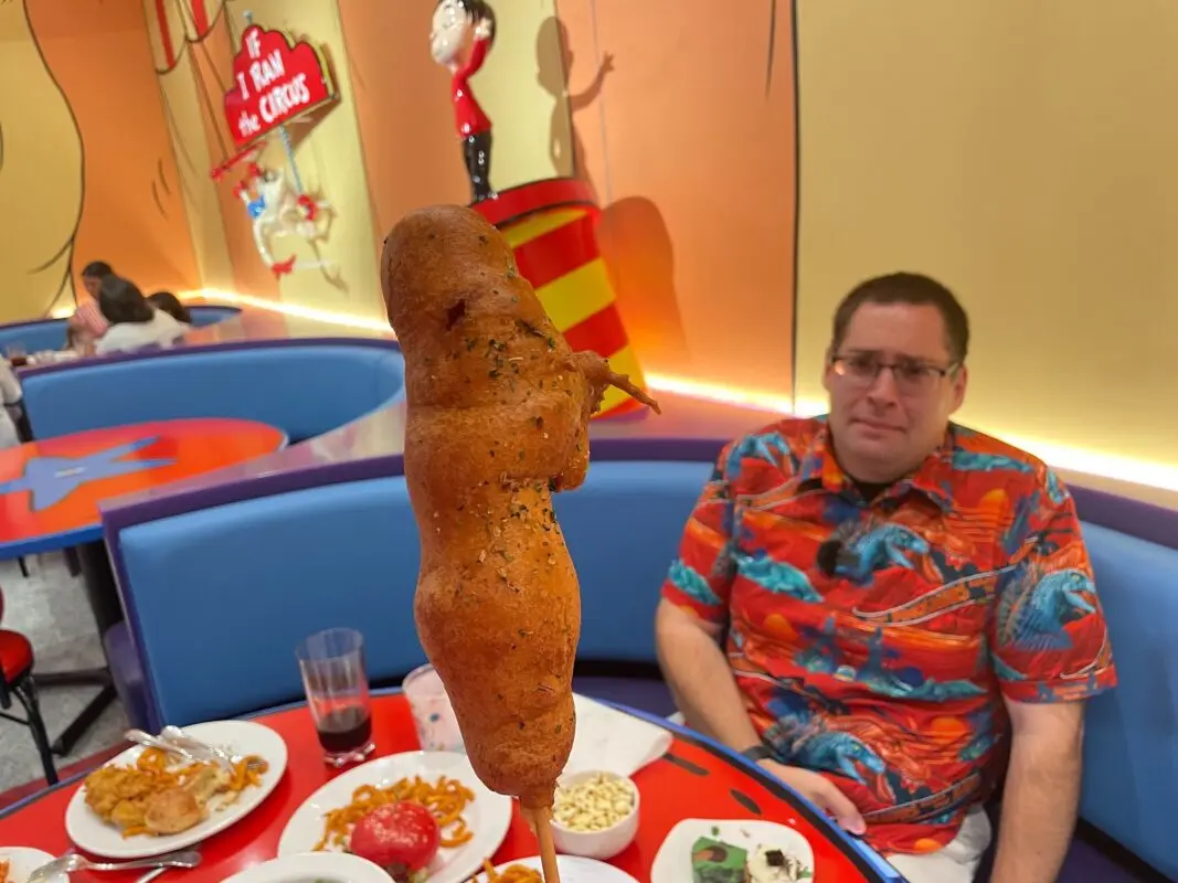 A wide shot of the Contorted Corn Dog with Tom Corless in the background with an uneasy expression