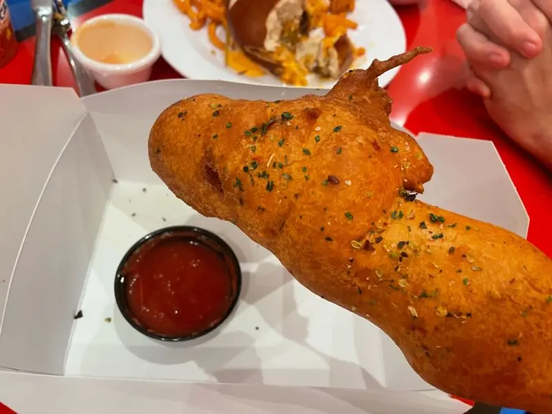 A closeup of the Contorted Corndog and a ramekin of marinara sauce