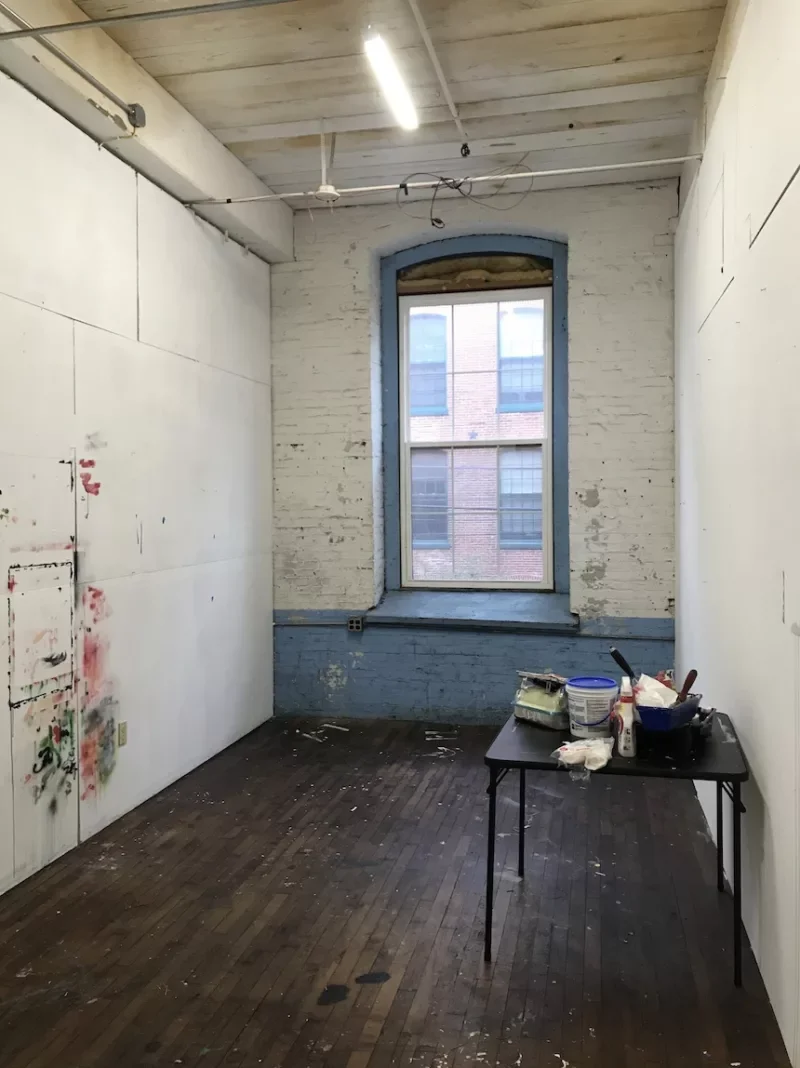Libby Rosa starts Peep Projects in 2020, with a peep hole in the door to see in. Why, you ask? 4 A long narrow room in need of some love and attention. The white paint on the far brick wall is coming off, the left wall has daubs of paint in red and green leftover from an artist painting a piece on the wall.