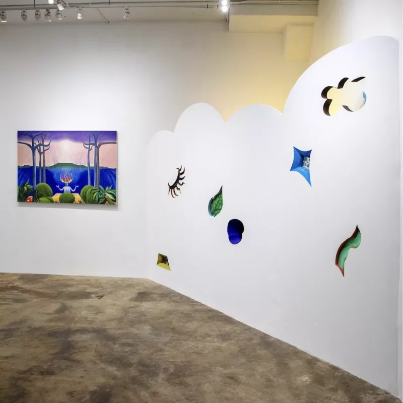 Libby Rosa starts Peep Projects in 2020, with a peep hole in the door to see in. Why, you ask? 7 A gallery installation shows a partial wall with a scalloped top edge on the right, with small surreal window-like cut outs into the wall that take the shape and color of a leaf in one instance and in others, something abstract. Behind the scalloped wall is a yellow light emanating.