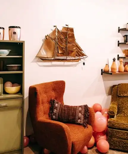 Vintage tufted chair with pillow and a brass ship decor piece on the wall.