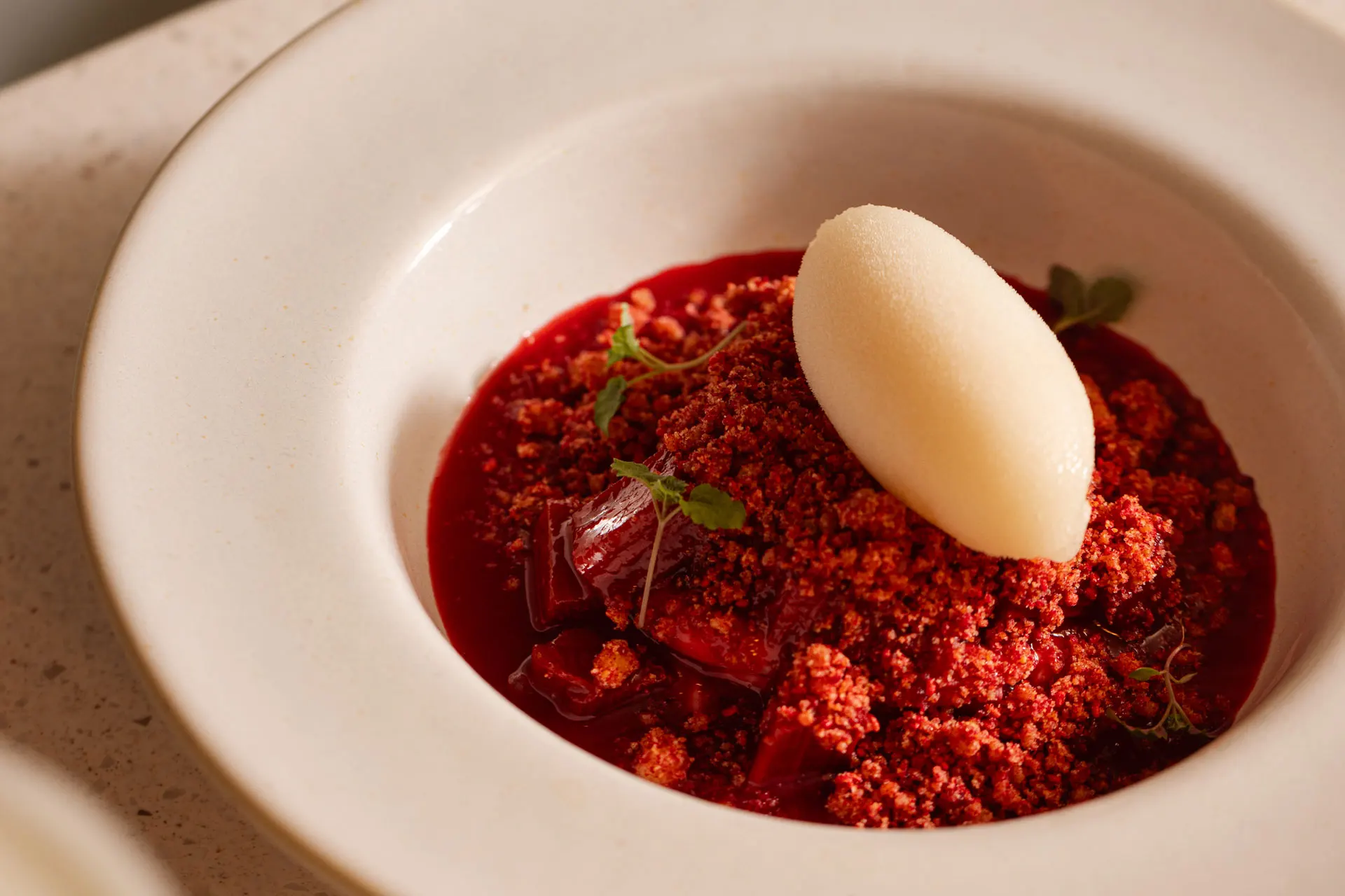 Bowl of poached rhubarb topped with white port sorbet.