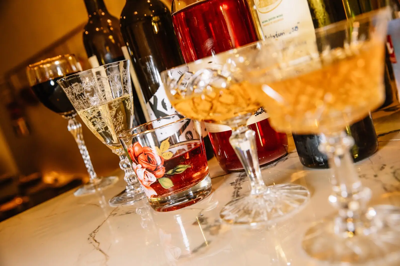 Mismatched glasses of wine atop a bar.