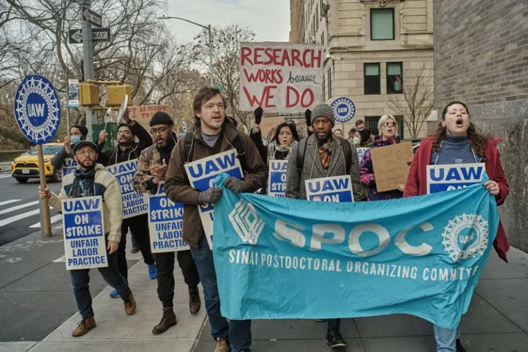 Demonstrators march through the streets holding banners and signs during strike action by the Sinai Postdoctoral Organizing Committee