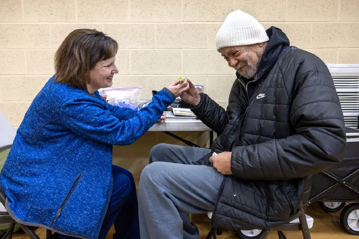 A man in a coat and winter cap reaches across a table and touches the hand of a woman in a coat. Both smile at one aother.