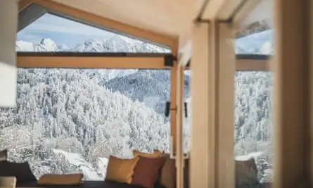 A cosy and modern interior with beige and brown scatter cushions on a sofa, looking out through a huge window on to the snowy valley.