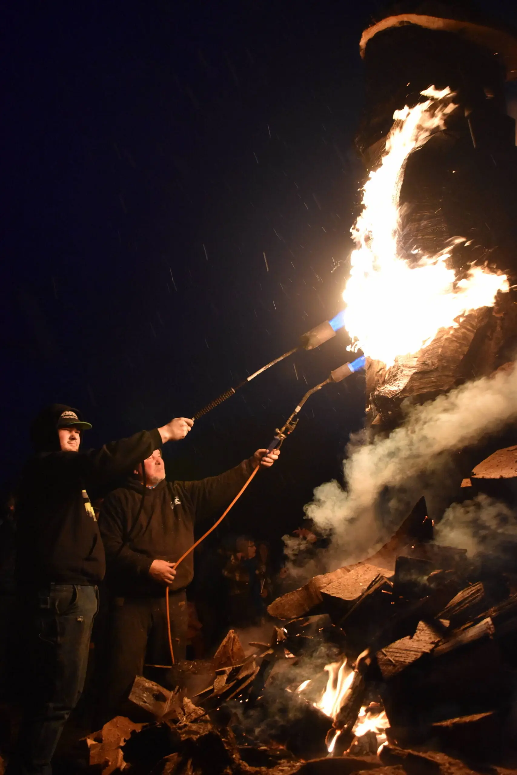 Volunteers supply the heat in an attempt to inflame a giant wooden bear recently doused in rain on Saturday, Feb. 17. (Clayton Franke / The Daily World)