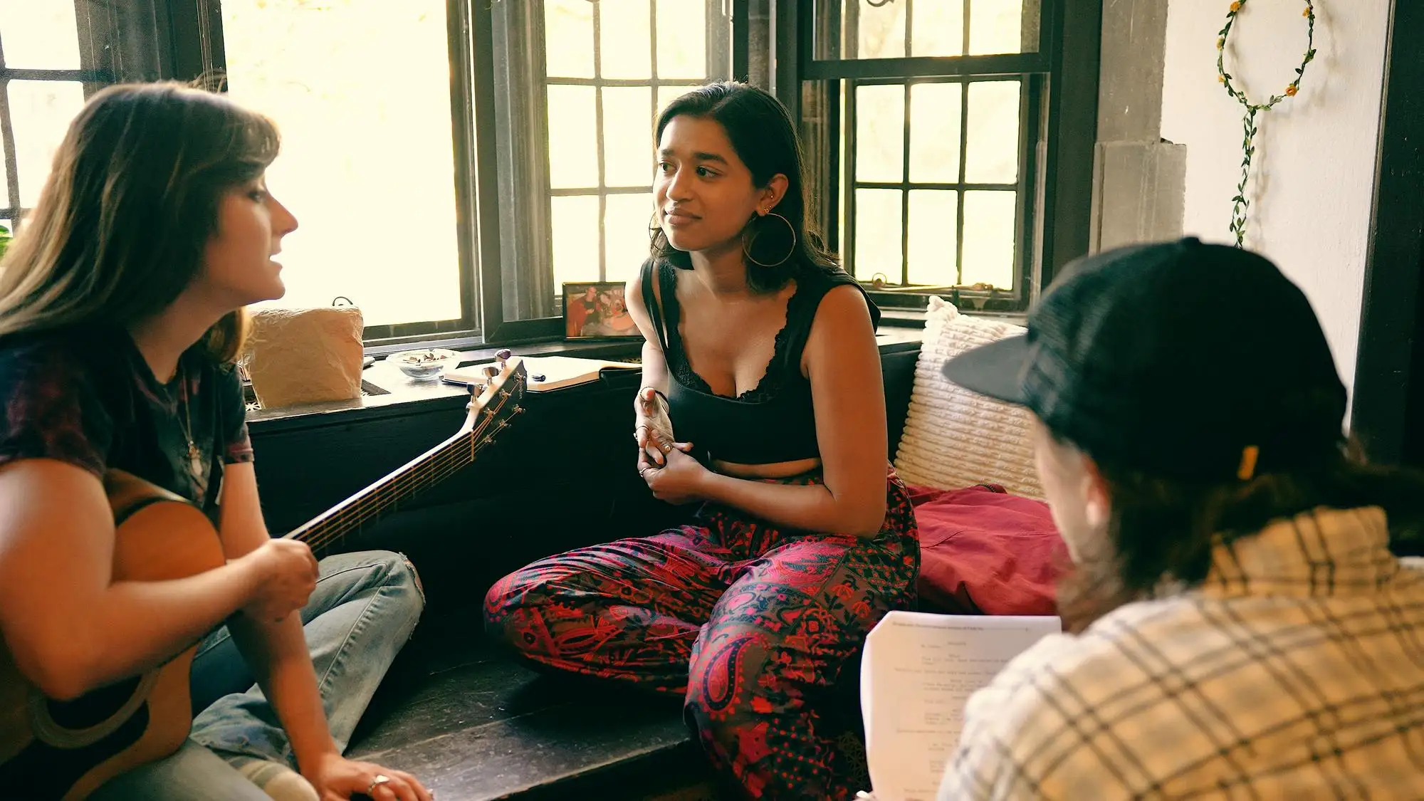 Two female students sit by a window in front of another student, holding a script. 