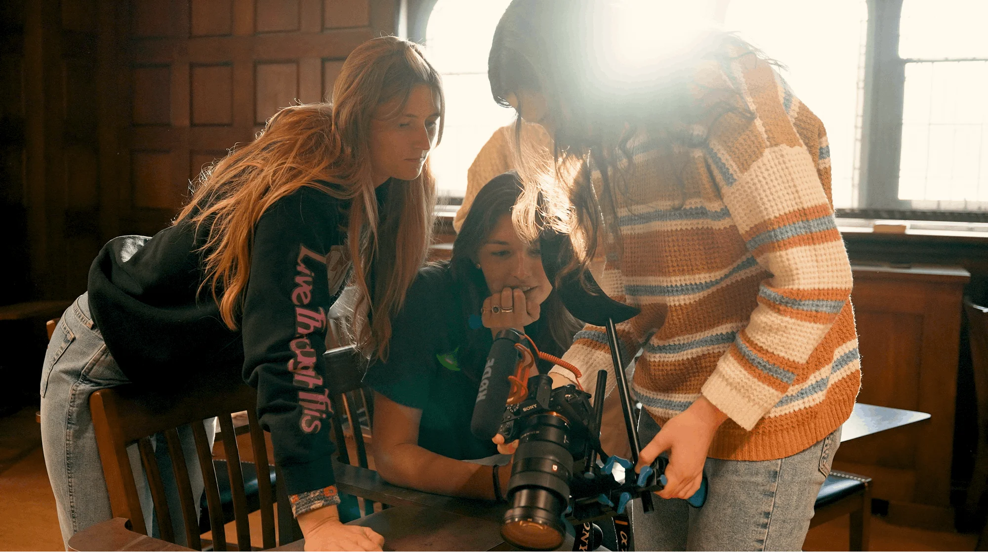 Three female students look at a recording in a camera.