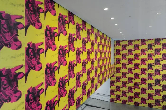 Andy Warhol’s ‘Cow’: dozens of reproductions of pink cow heads against a yellow background on the walls of MoMA’s ground-floor lobby