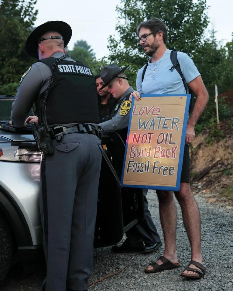 Peter Kalmus holding a protest board looks on as Virginia State Police take down his information