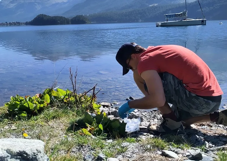 A citizen scientist wears protective gloves and takes samples from a fresh water lake.