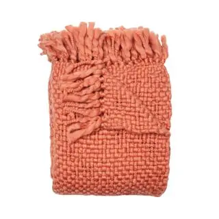 A folded coral chunky knit throw blanket with tasseled detailing