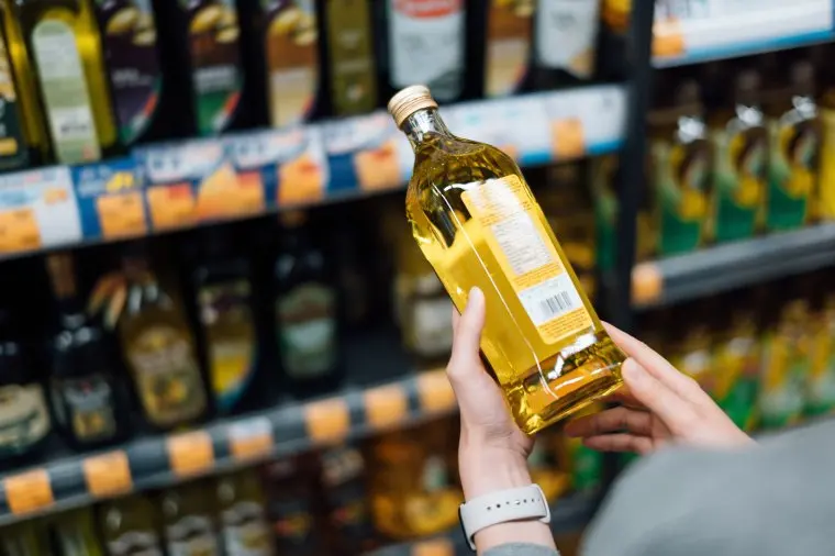 Close up of young woman grocery shopping in a supermarket. Standing by the aisle, holding a bottle of organic cooking oil, reading the nutritional label and checking ingredients at the back